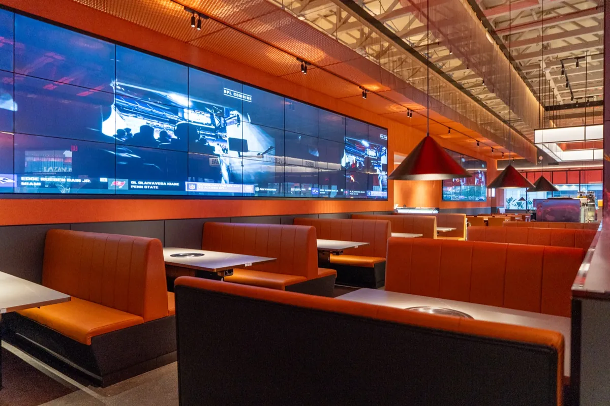 Dining area with large screens and orange booth seating at Kazan BBQ South Gate